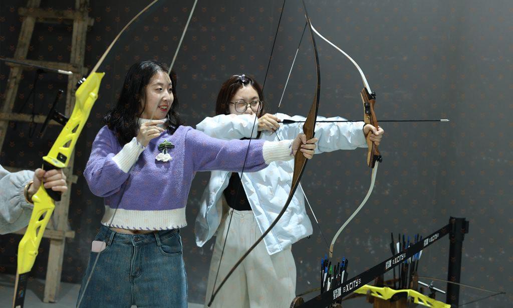 顾客在数字运动馆模拟射箭区拉弓瞄准，两人同场进行射箭竞技